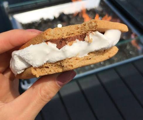 A gourmet s'more held in front of a rooftop firepit